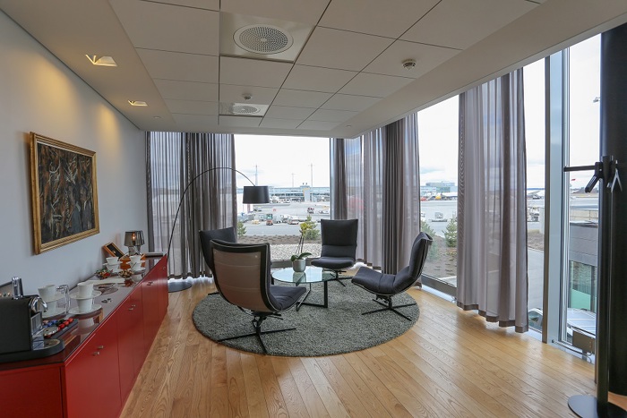 Lyst møterom med utsikt over flyplass, elegant innredet med moderne stoler, et rundt bord og kunst på veggen.